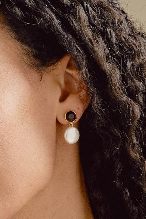 Woman wearing a necklace and earrings against a neutral background
