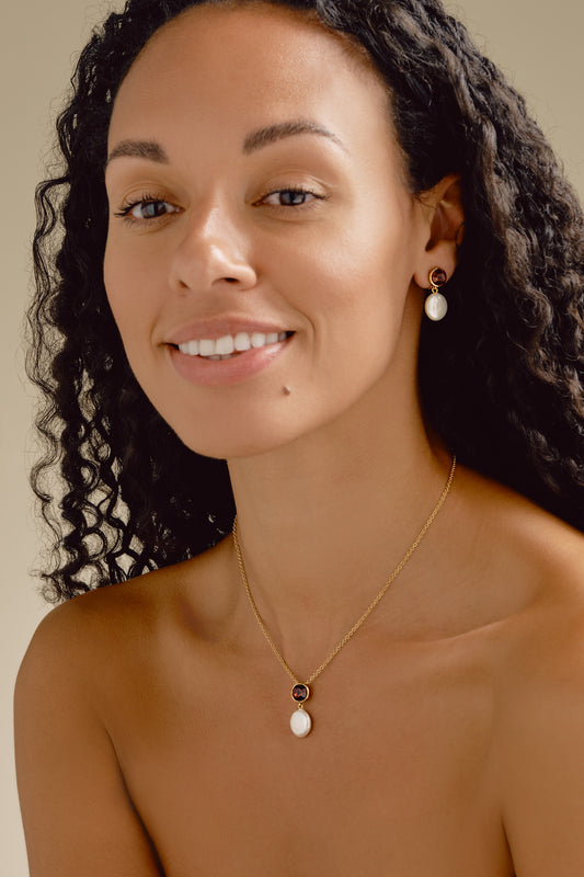 Woman wearing a gold necklace with a pendant against a neutral background