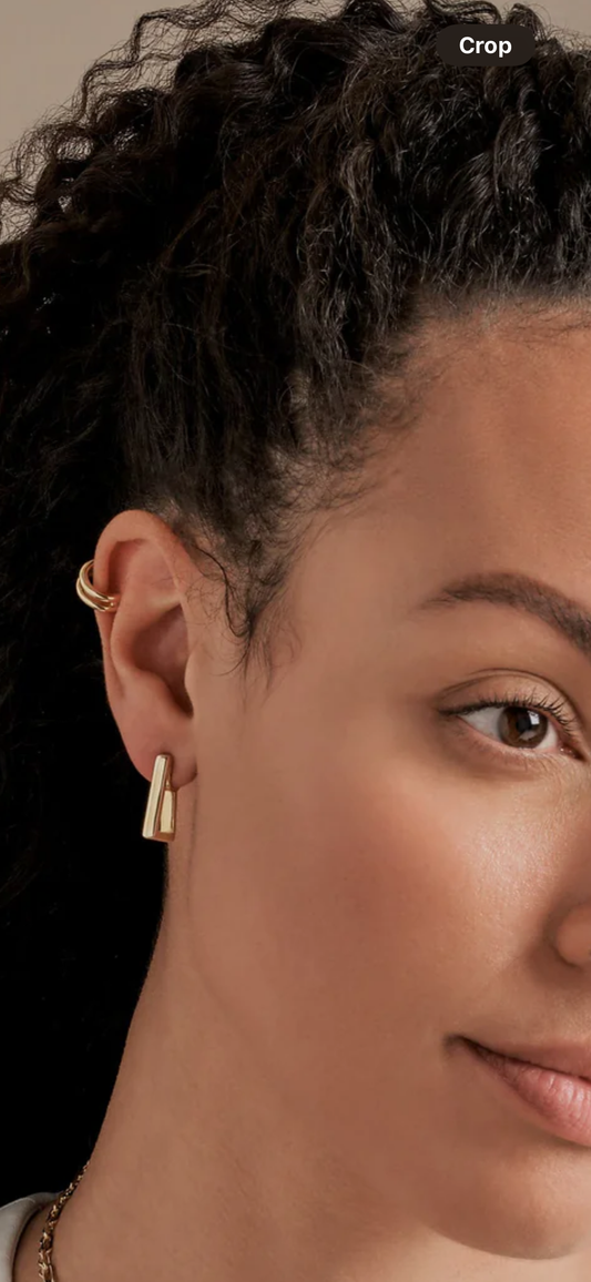 Close-up of a person wearing a gold earring with a neutral background