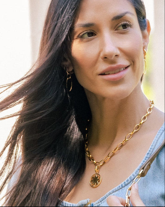 Woman with long dark hair and gold necklace outdoors