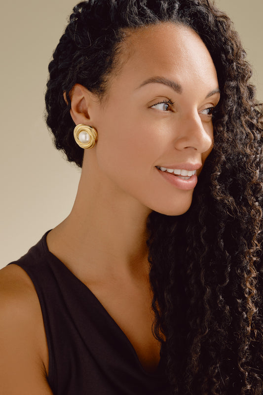 Woman wearing gold earrings with a beige background