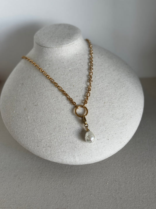 Gold necklace with a pearl pendant on a gray stand against a gray background
