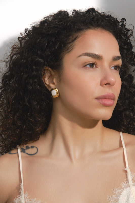 Woman with curly hair wearing gold earrings against a neutral background