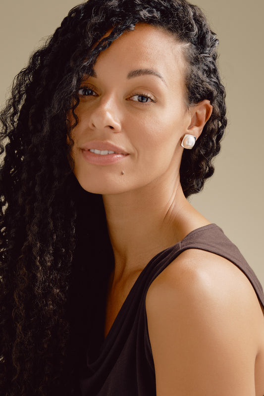 Woman with styled hair and earrings against a neutral background