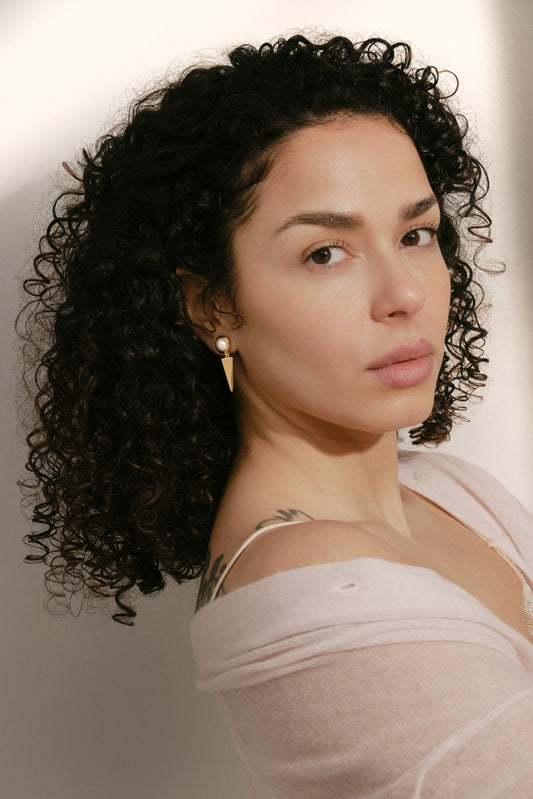 Woman with curly hair wearing a white top against a neutral background and gold clip on earrings
