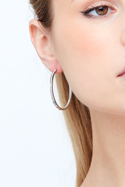 Close-up of a person wearing a silver hoop earring on a white background