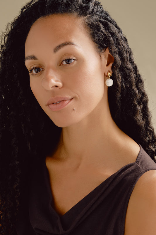 Woman with long braided hair wearing a black top wearing coin pearl clip on earrings