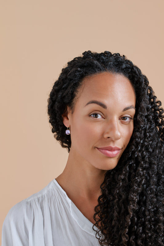 Woman with styled hair against a beige background in Violet crystal earrings