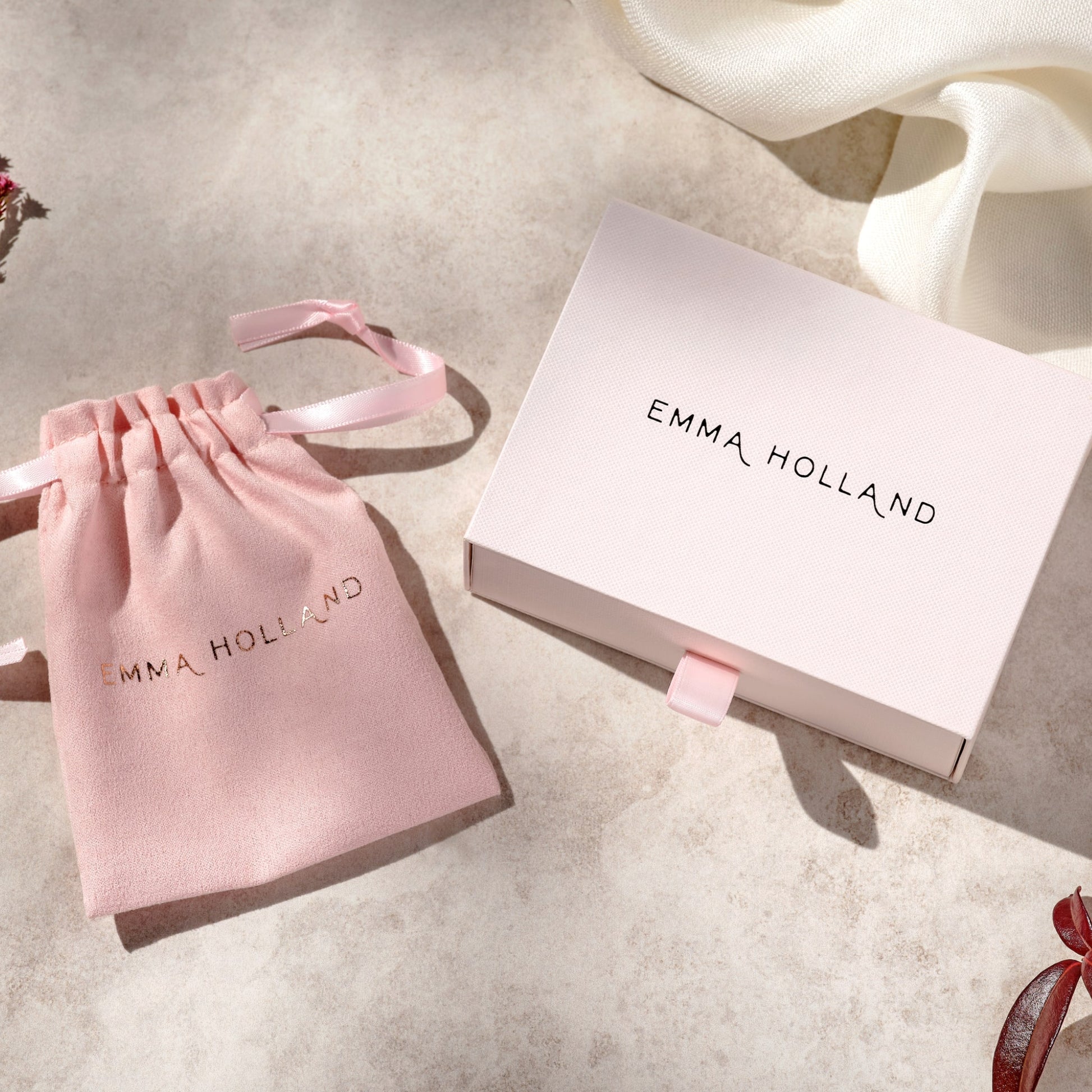 Pink jewelry pouch and box with 'Emma Holland' branding on a light surface.
