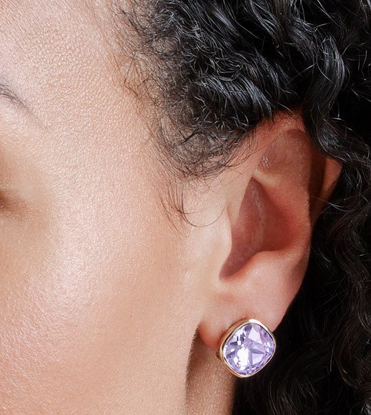 Close-up of an ear wearing a gold earring with a purple gemstone.