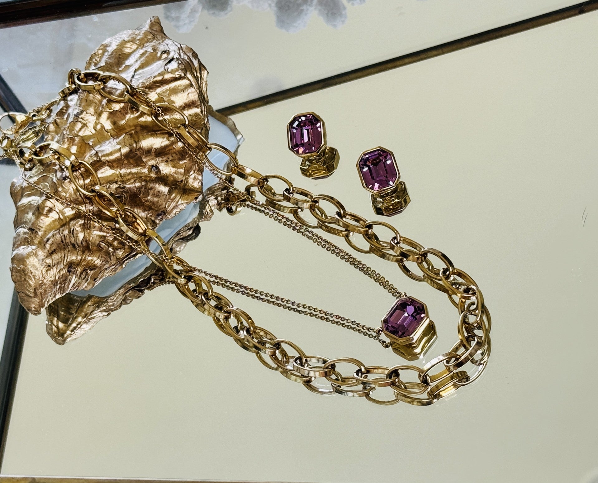 Gold necklace with purple gemstones and matching earrings on a reflective surface