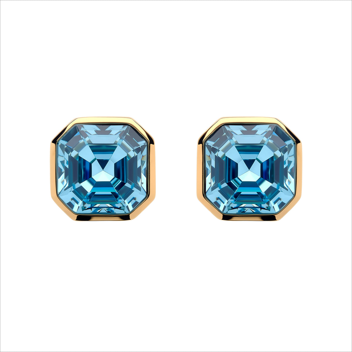 A pair of stud earrings featuring large, faceted light blue gemstones in a square bezel setting with polished gold-toned metal borders, shown against a plain white background.