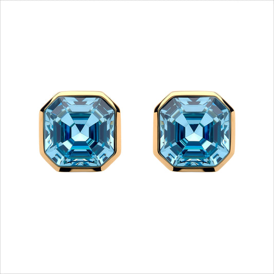 A pair of stud earrings featuring large, faceted light blue gemstones in a square bezel setting with polished gold-toned metal borders, shown against a plain white background.