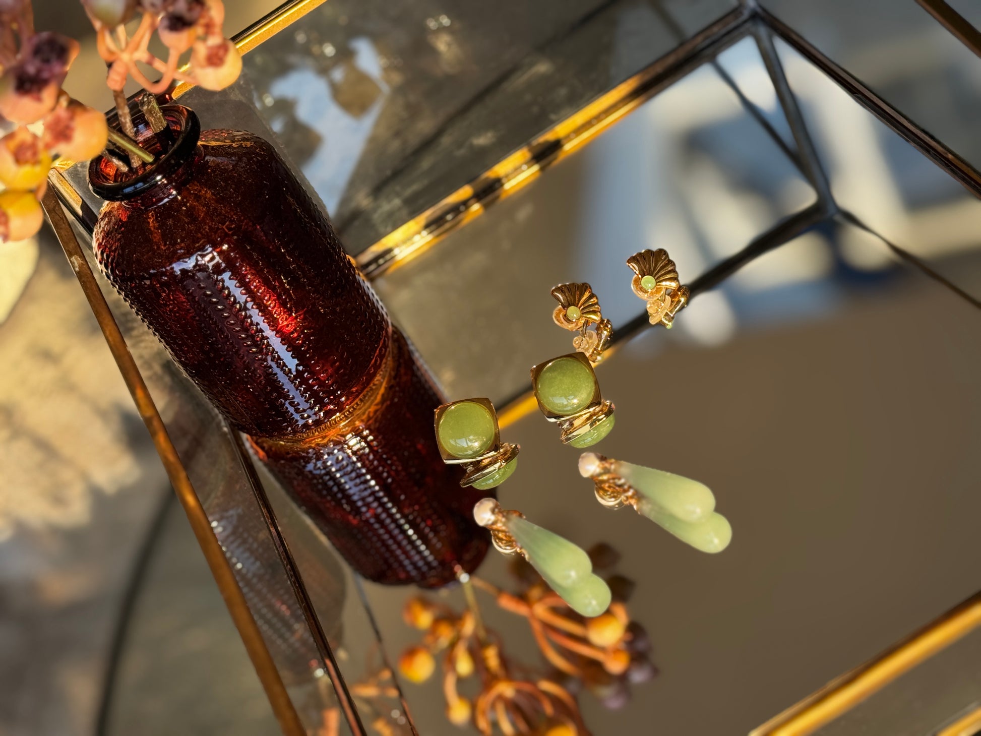 Brown bottle and green beaded earrings on a reflective surface