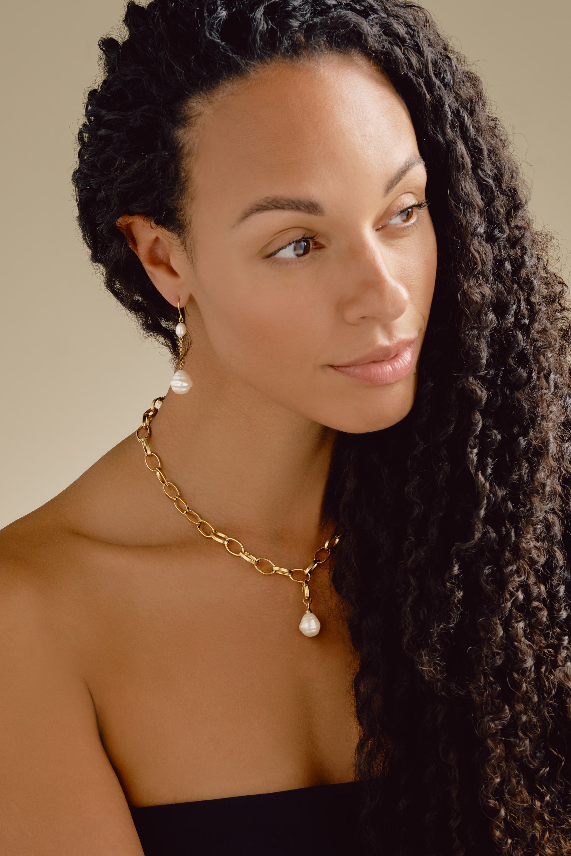 Woman wearing a gold necklace with pearl pendant against a neutral background