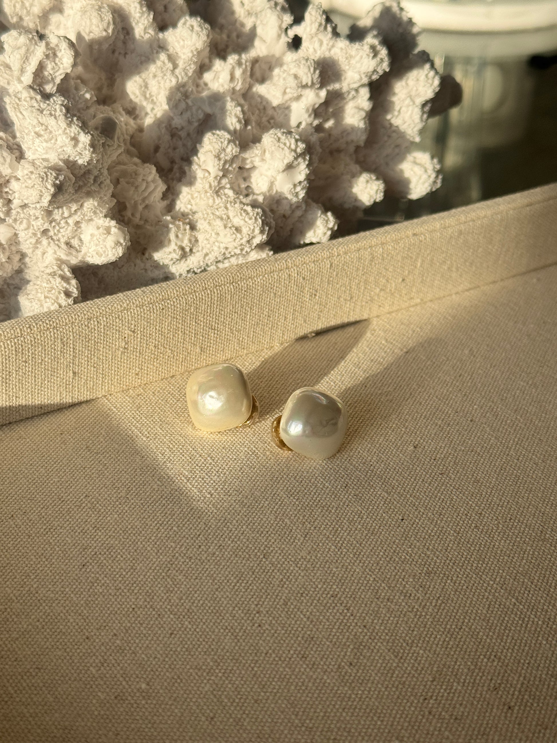 Pearl earrings on a textured beige surface with a blurred background