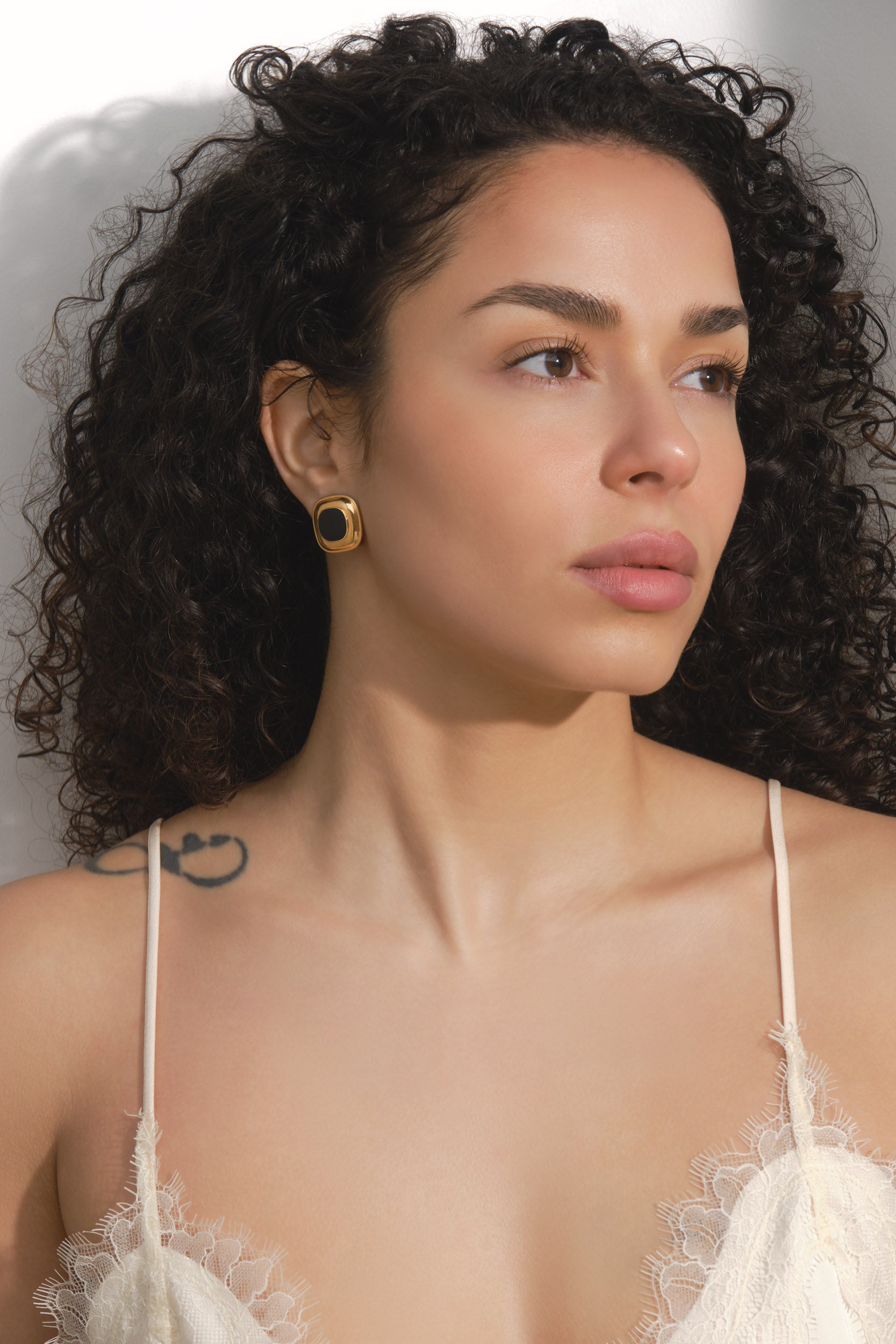 Woman wearing a white lace top with a neutral background wearing clip on earrings
