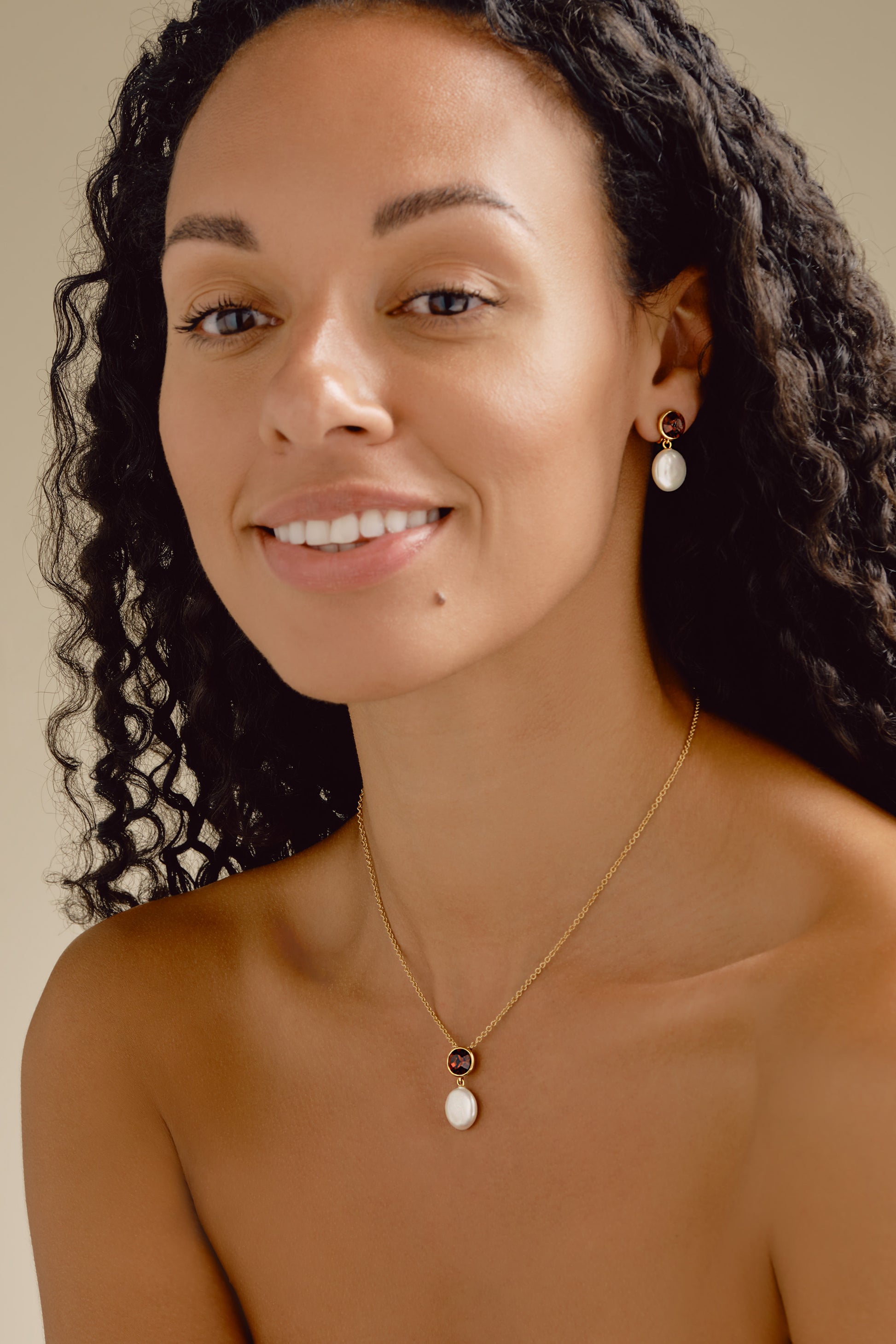 Woman wearing a gold necklace with a pendant against a neutral background