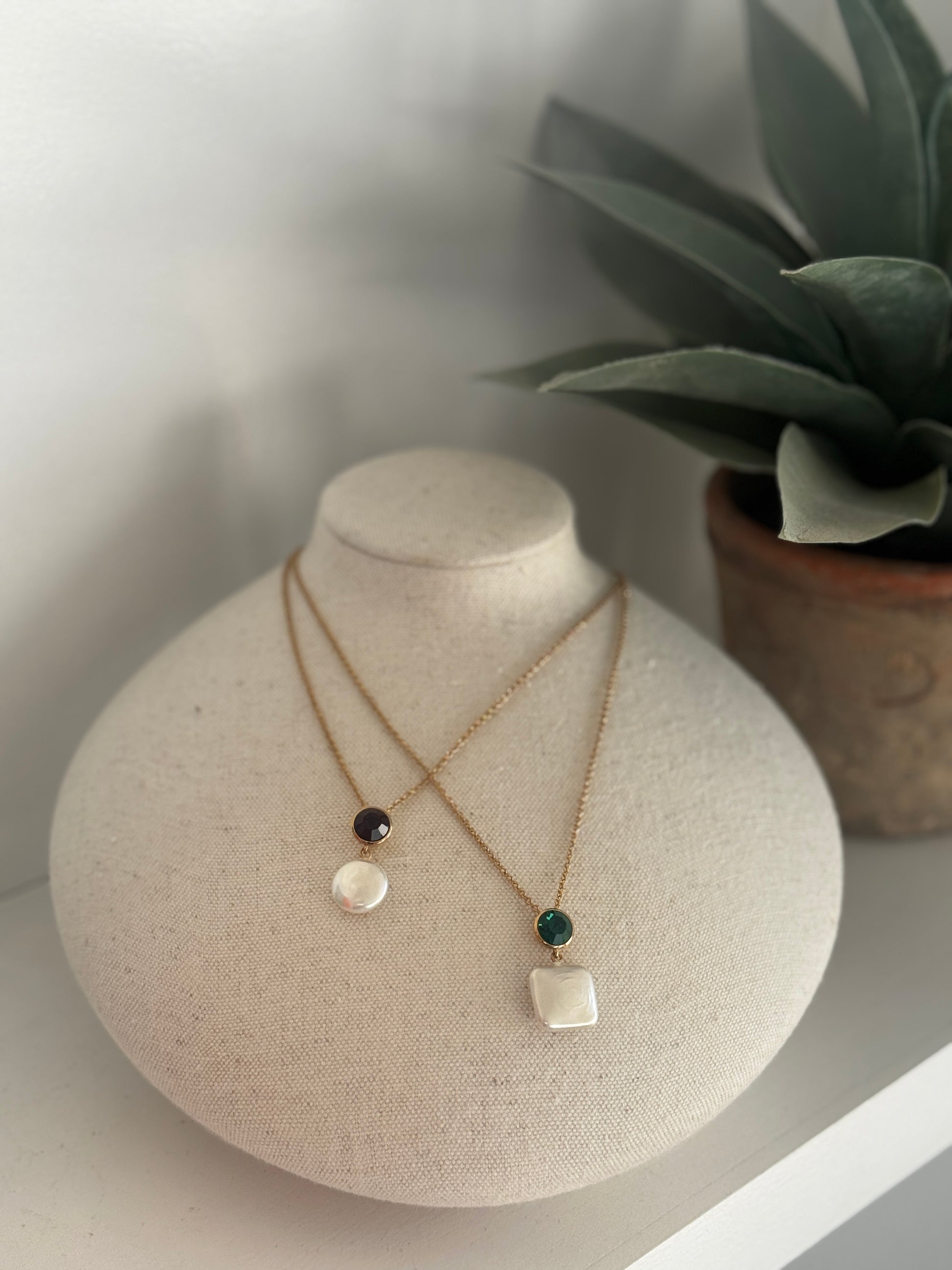 Necklace with pendant on a mannequin bust with a plant in the background