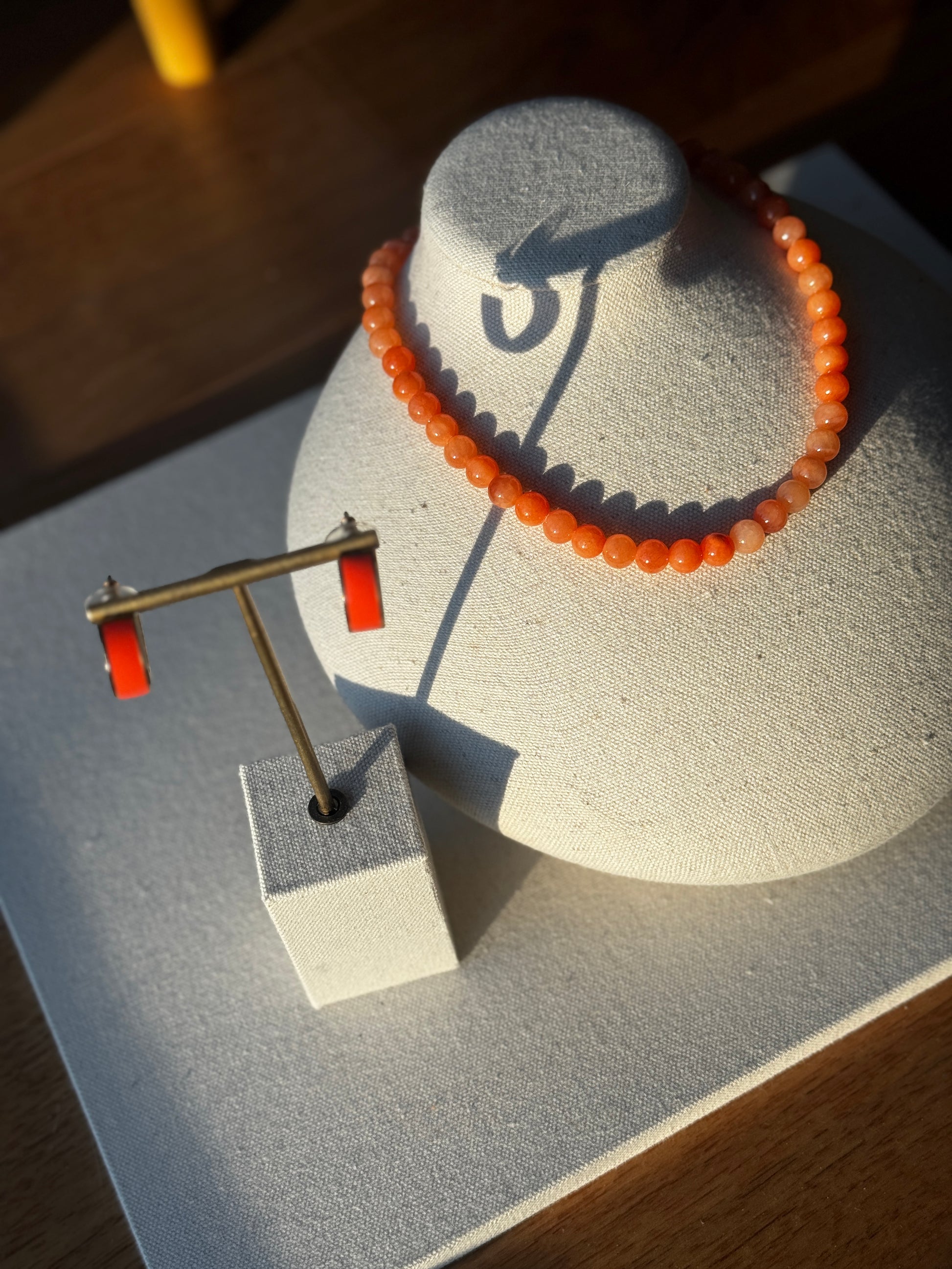 Orange beaded bracelet on a gray stand with earrings on a matching stand.
