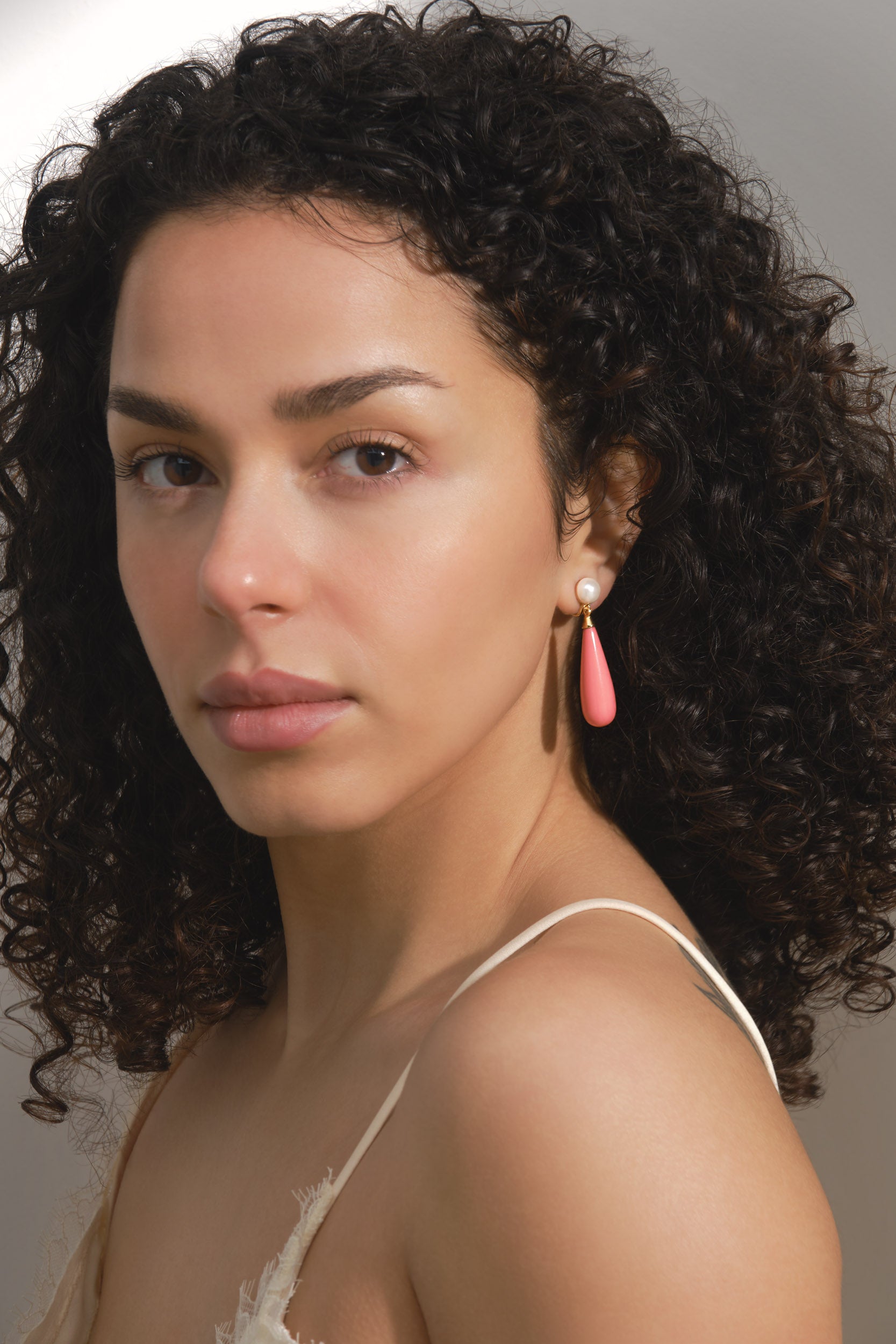 Woman with curly hair wearing pink earrings against a neutral background