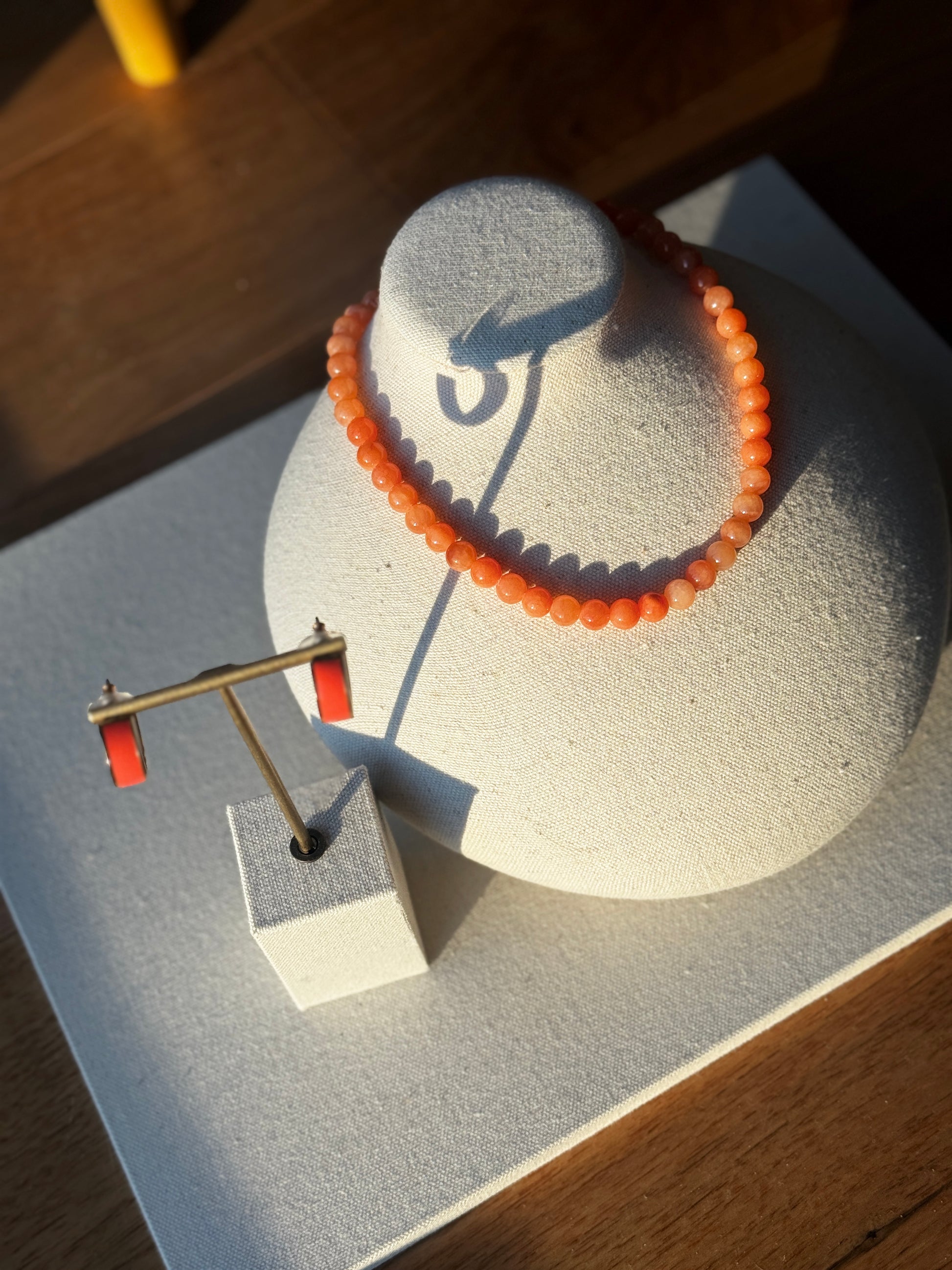 Orange beaded bracelet on a white circular stand with a wooden surface below
