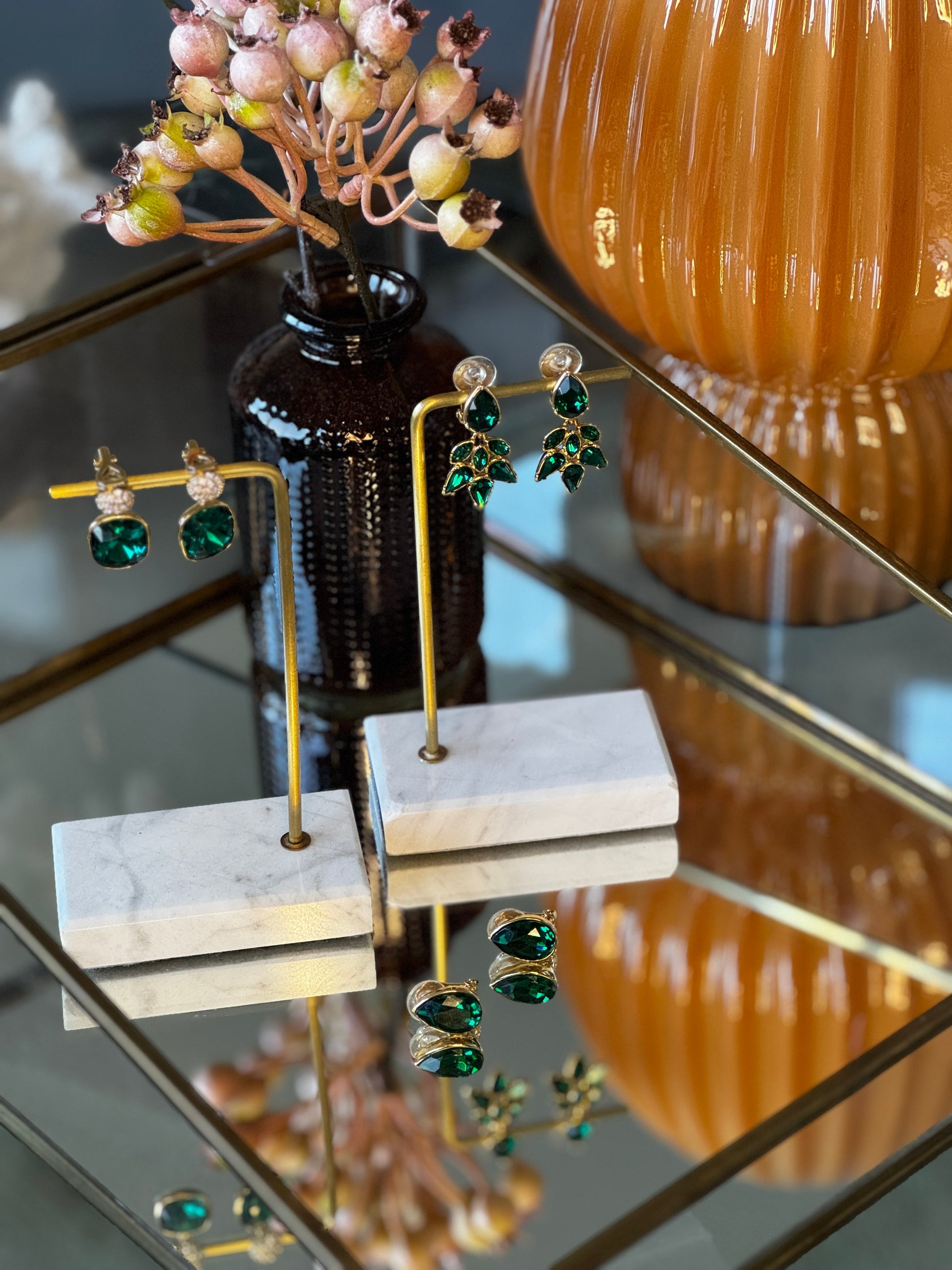Green gemstone earrings on display with a decorative vase in the background.