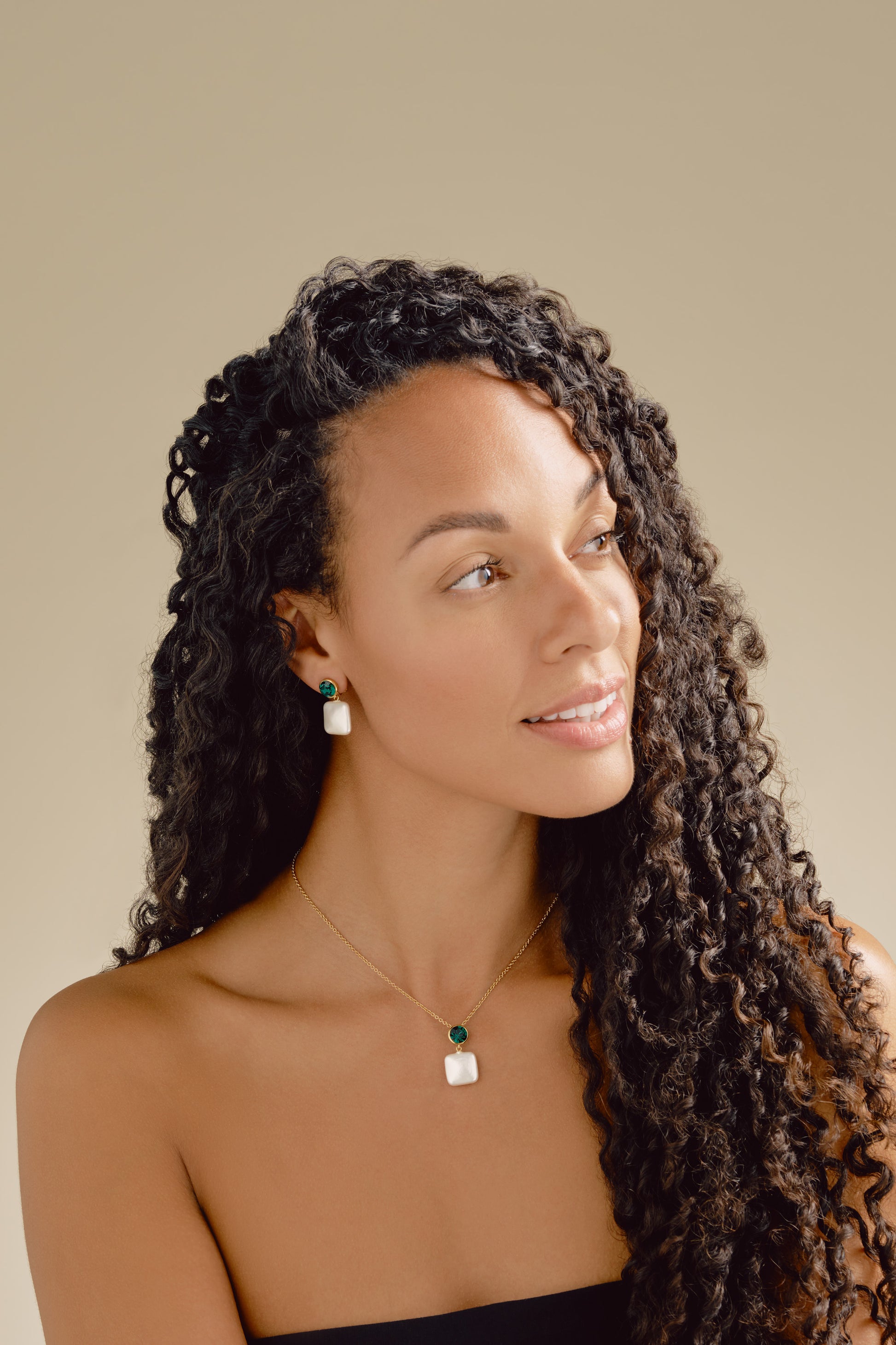 Woman with long, curly hair wearing earrings and a necklace against a neutral background