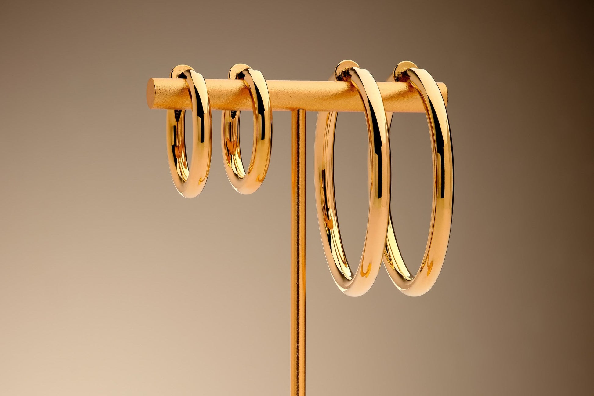 Gold hoop earrings on a stand against a brown background