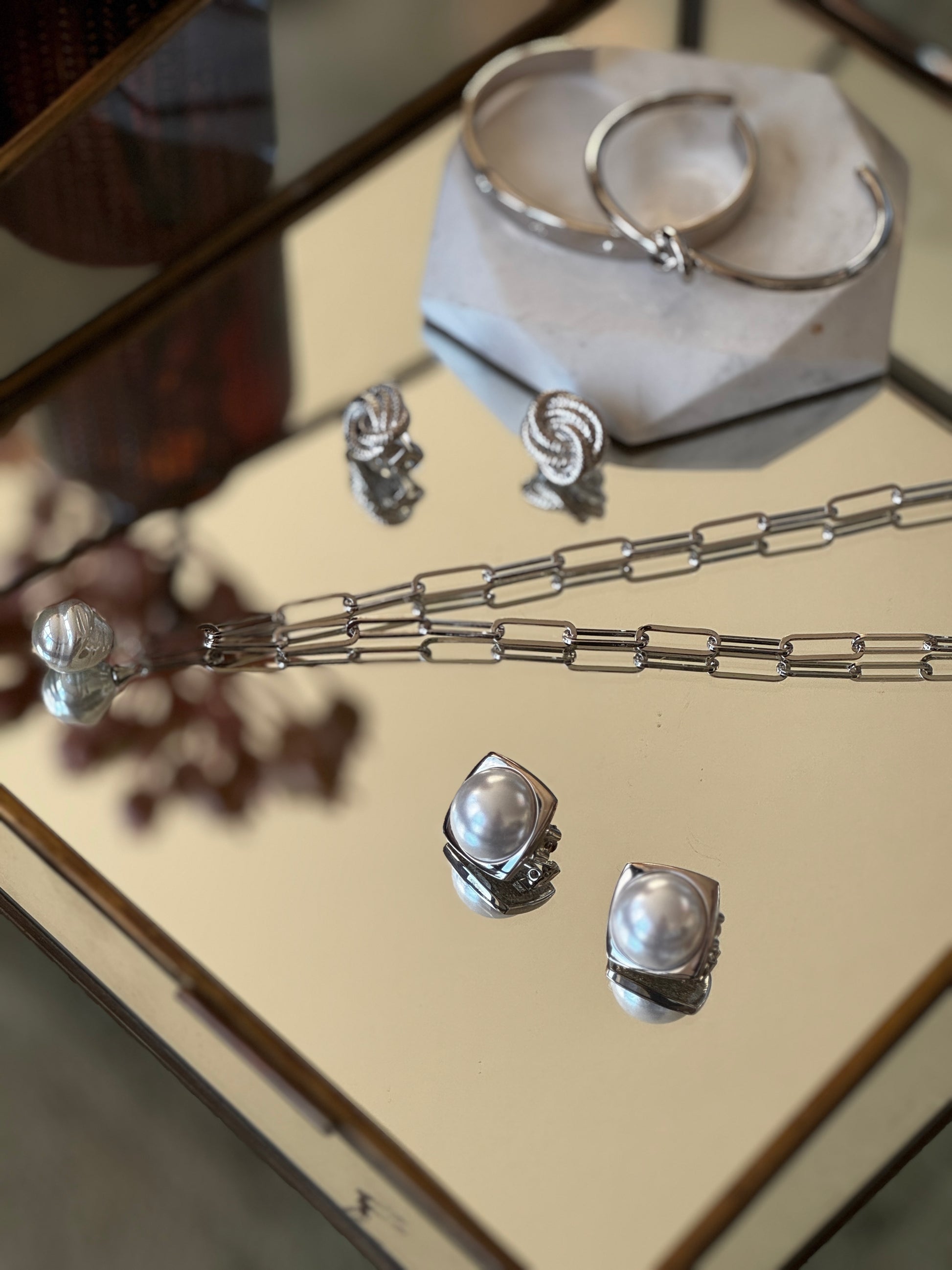 Silver jewelry set including necklace, earrings, and bracelet on a reflective surface.