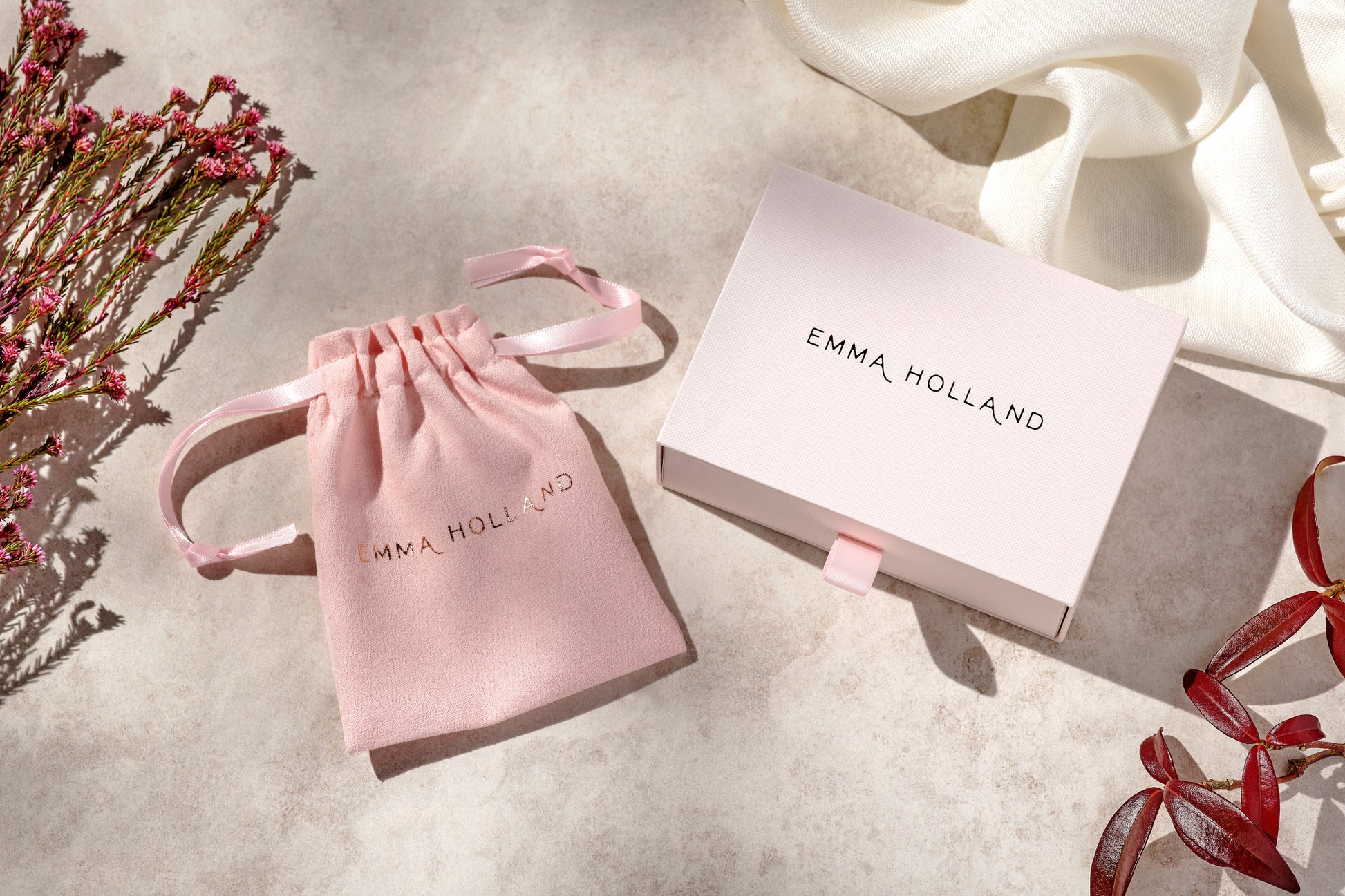 Pink drawstring bag and box with 'EMMA HOLLAND' branding on a light surface.