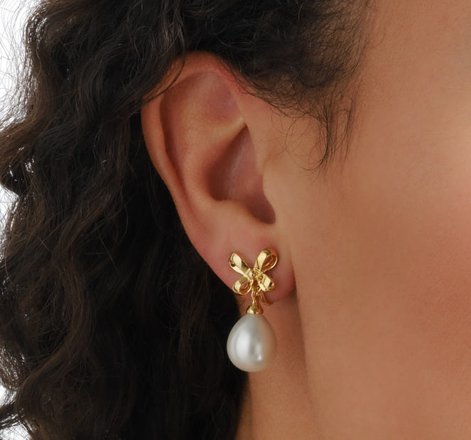 Gold earring with a pearl drop worn by a person
