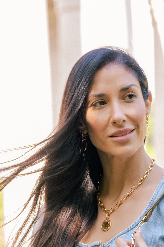 Woman with long dark hair and gold necklace outdoors