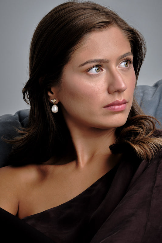 A model wearing gold heart and pearl earrings