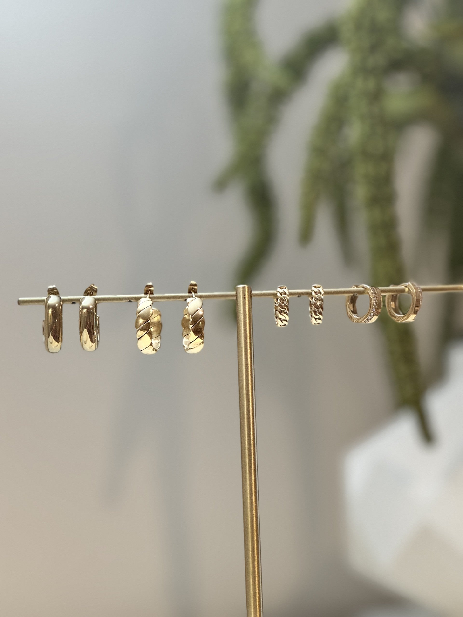 Set of gold hoop earrings on a stand with a blurred natural background