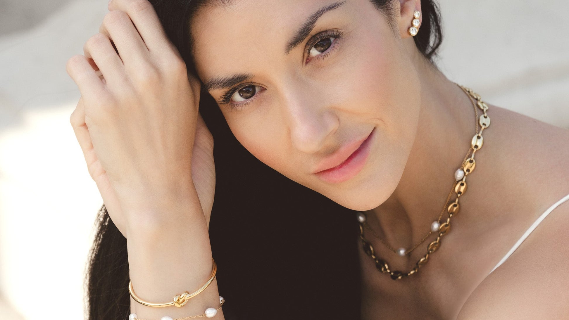 Woman wearing gold jewelry including a necklace, bracelet, and earrings.