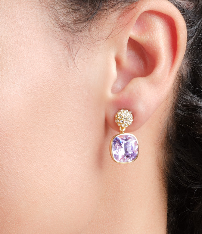 Close-up of an ear wearing a gold earring with a purple gemstone.