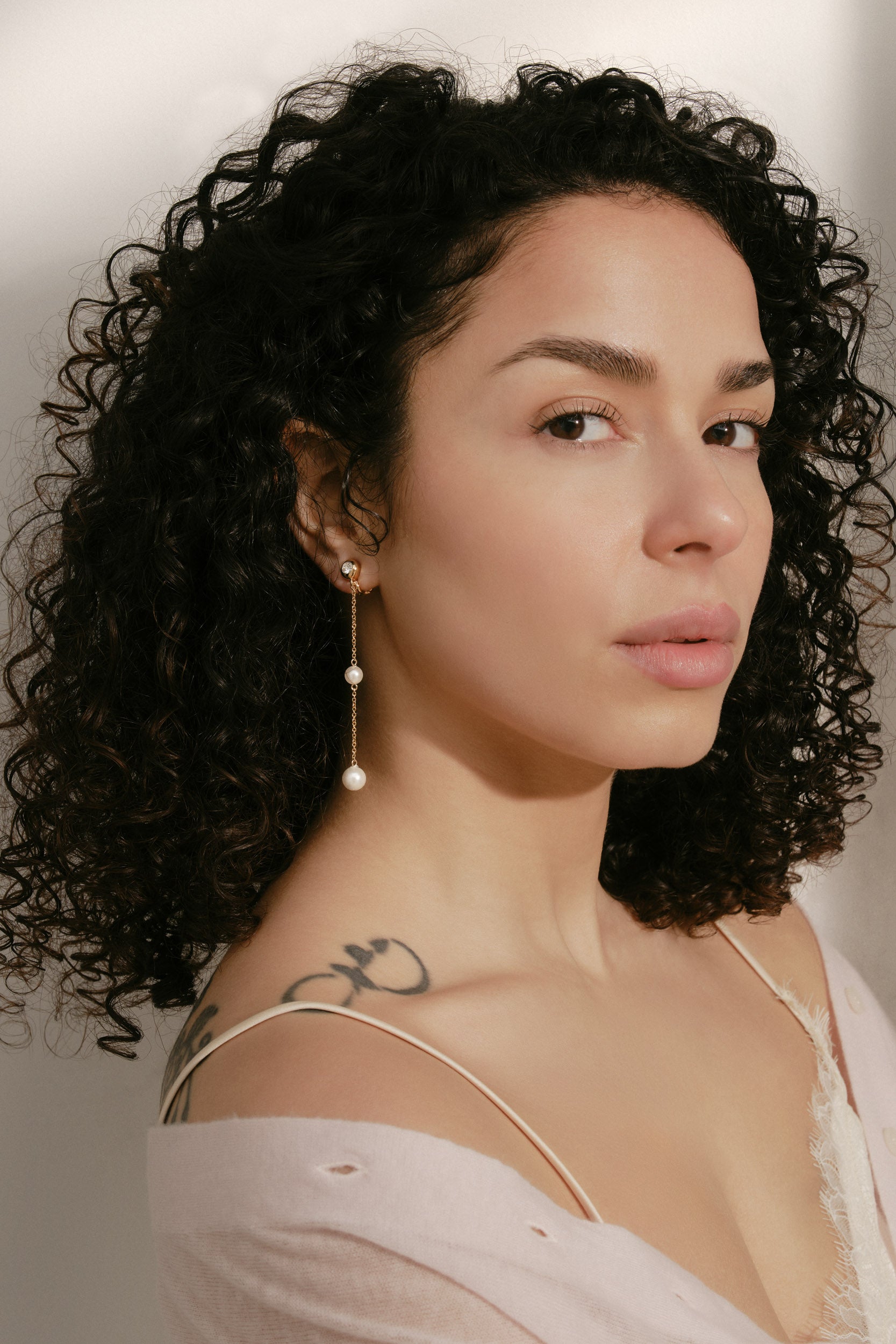 Woman with curly hair wearing gold and pearl earrings
