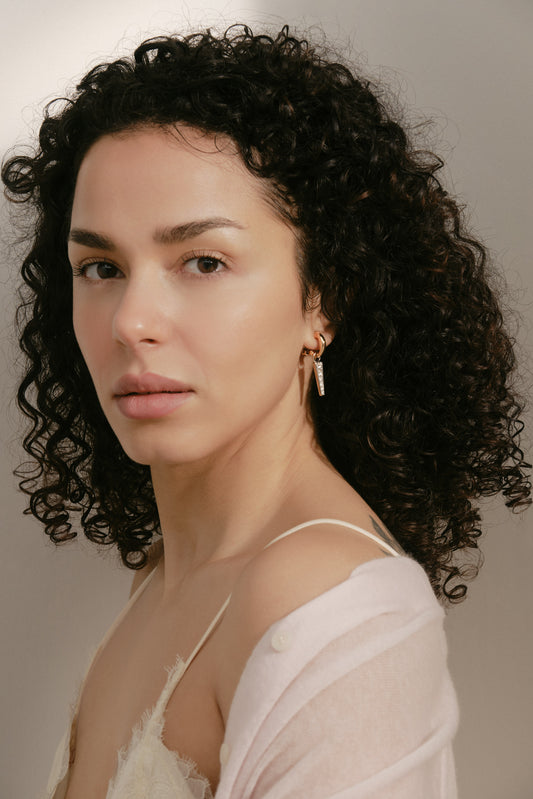 Woman with curly hair wearing a light-colored top against a neutral background