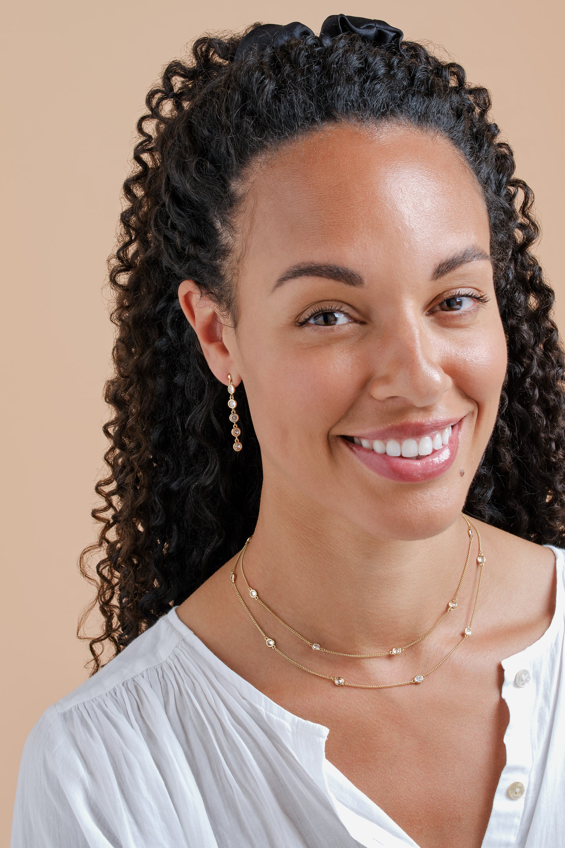 Woman with styled hair and jewelry against a beige background
