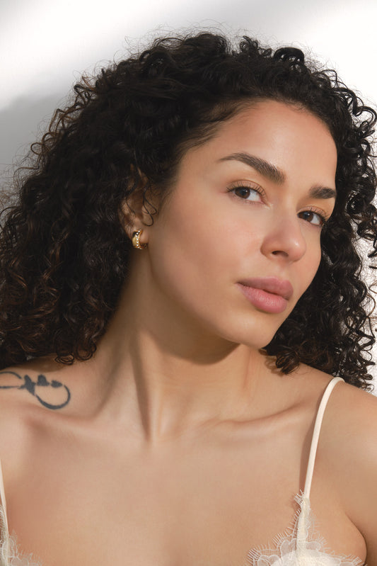 Woman with curly hair wearing a white lace top against a neutral background