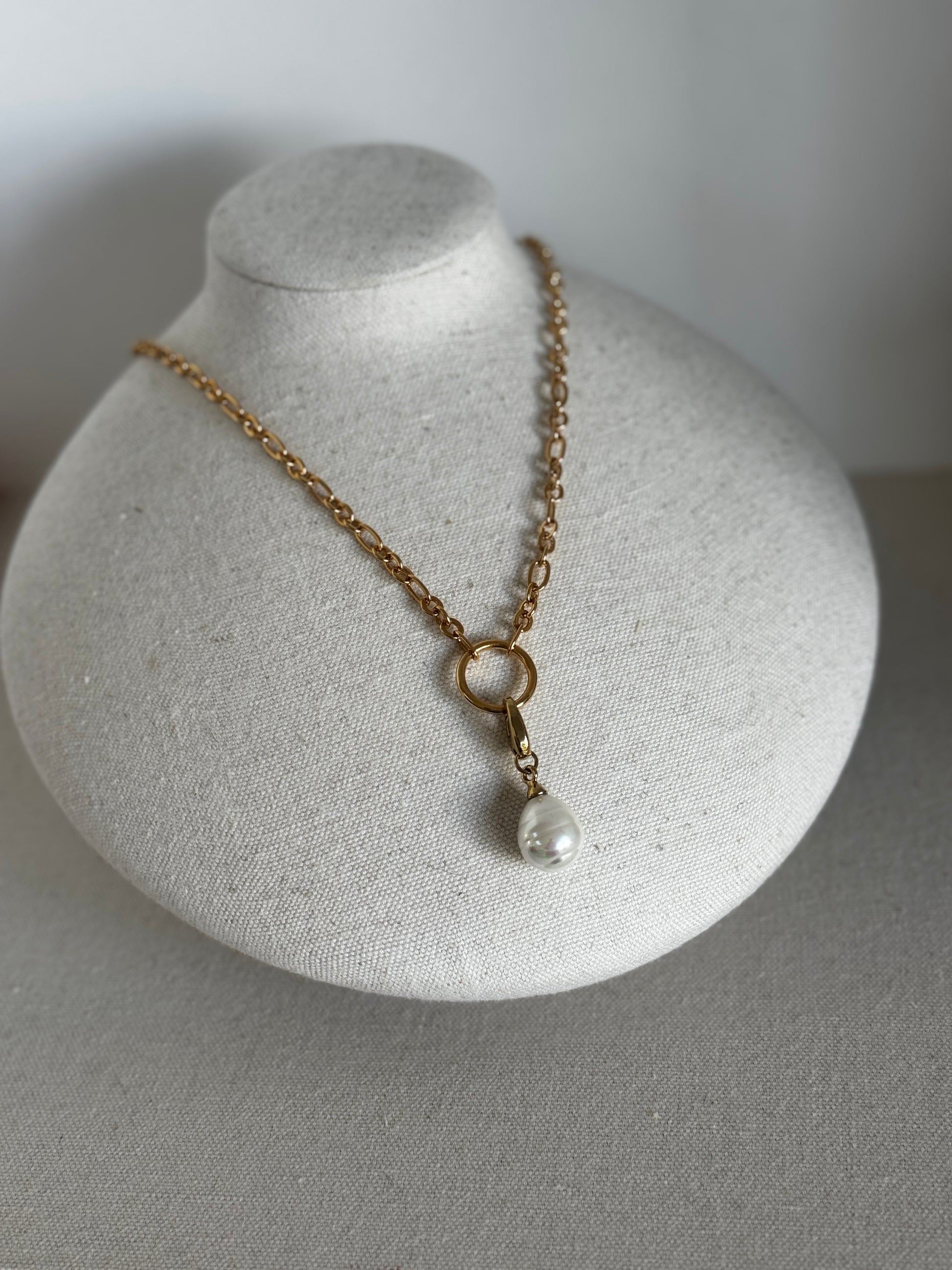 Gold necklace with a pearl pendant on a gray stand against a gray background