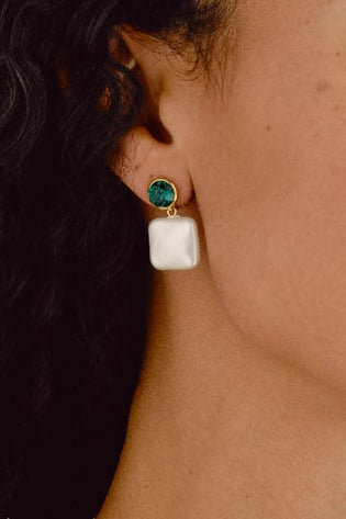 Woman with long, curly hair wearing earrings and a necklace against a beige background