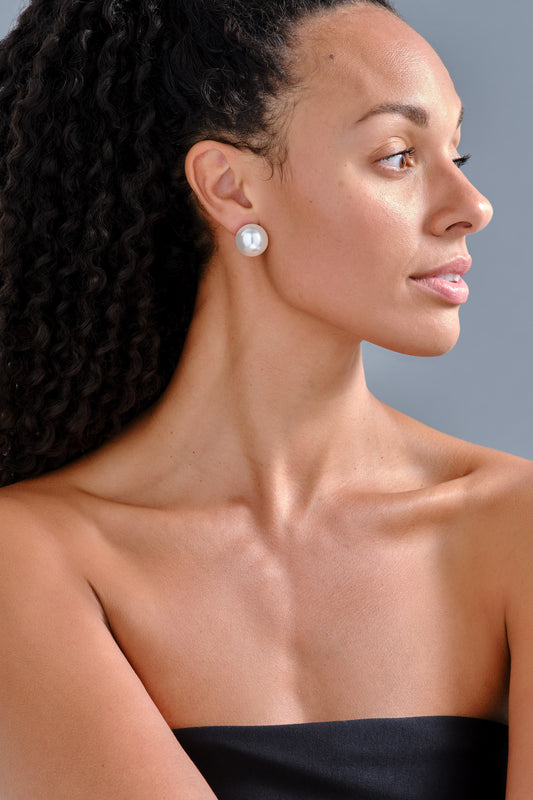 A model wearing large pearl clip earrings