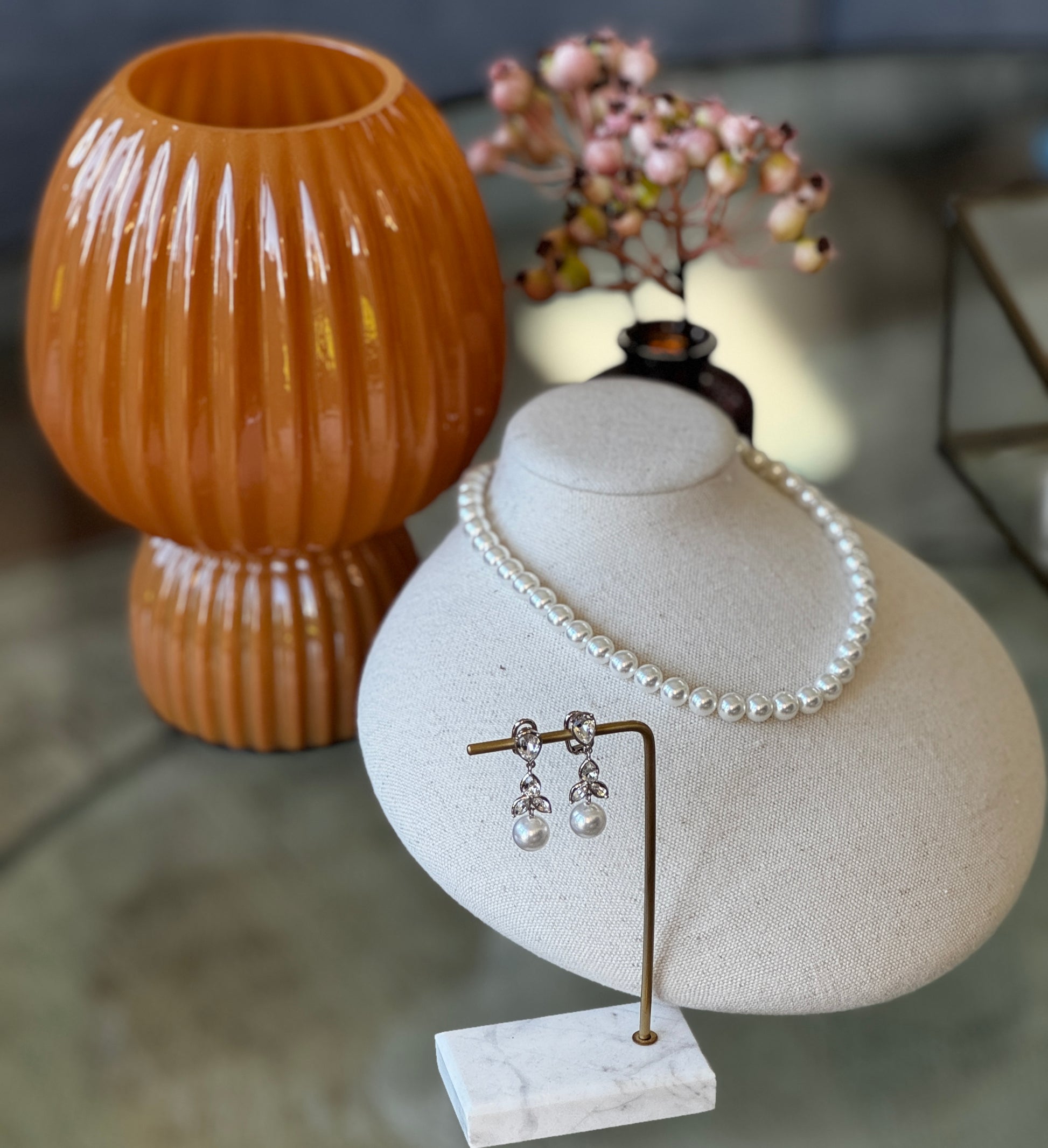 Pearl necklace and earrings on a white jewelry display with a brown textured vase in the background.