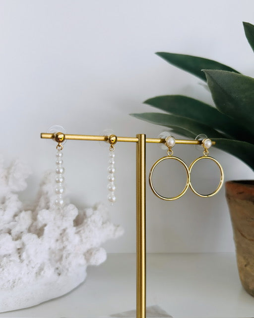 Gold earrings on a stand with a white background and plant