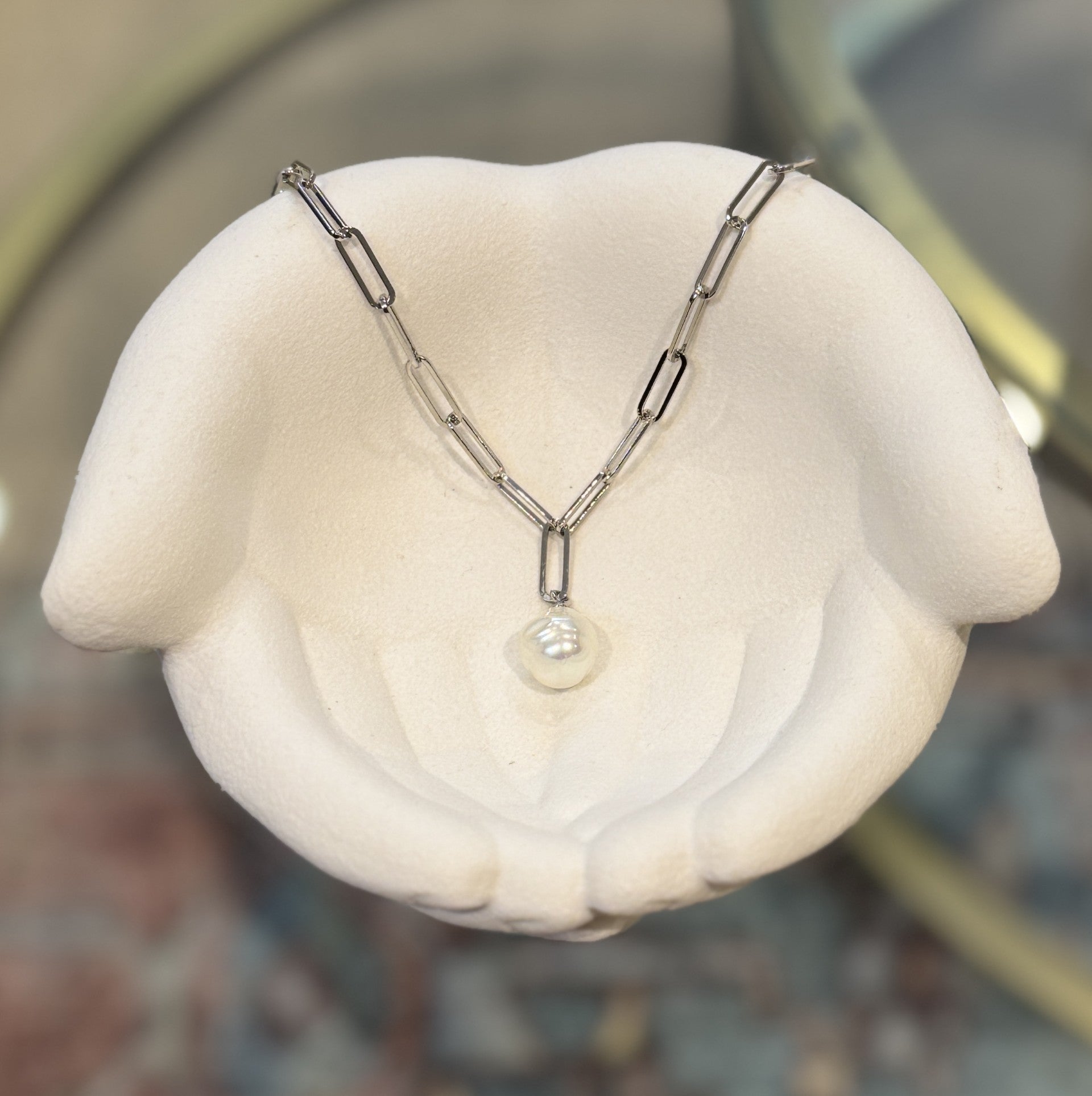 Silver necklace with a pearl pendant on a white stand