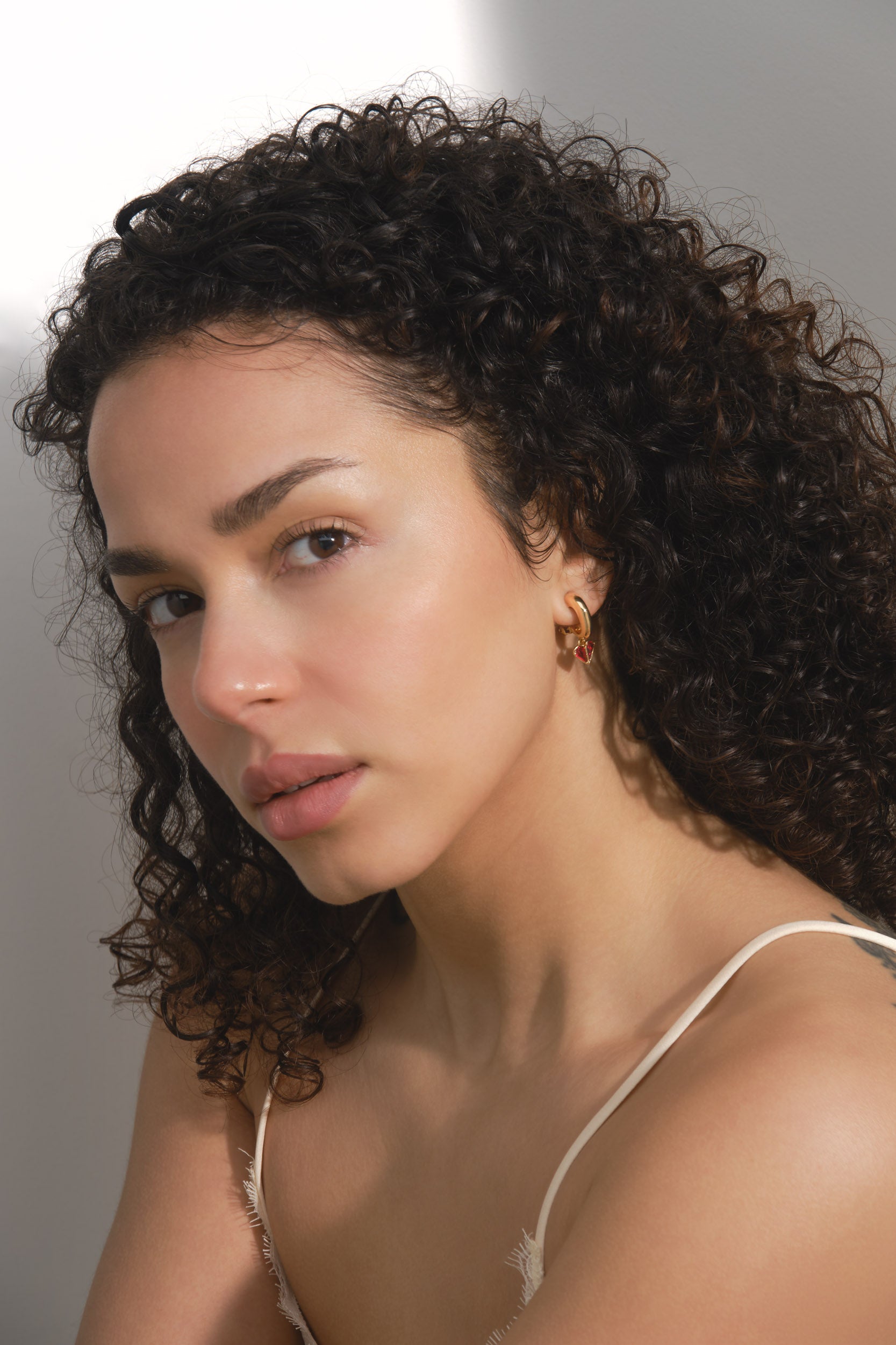 Woman with curly hair wearing a white top against a neutral background wearing Emma Holland earrings