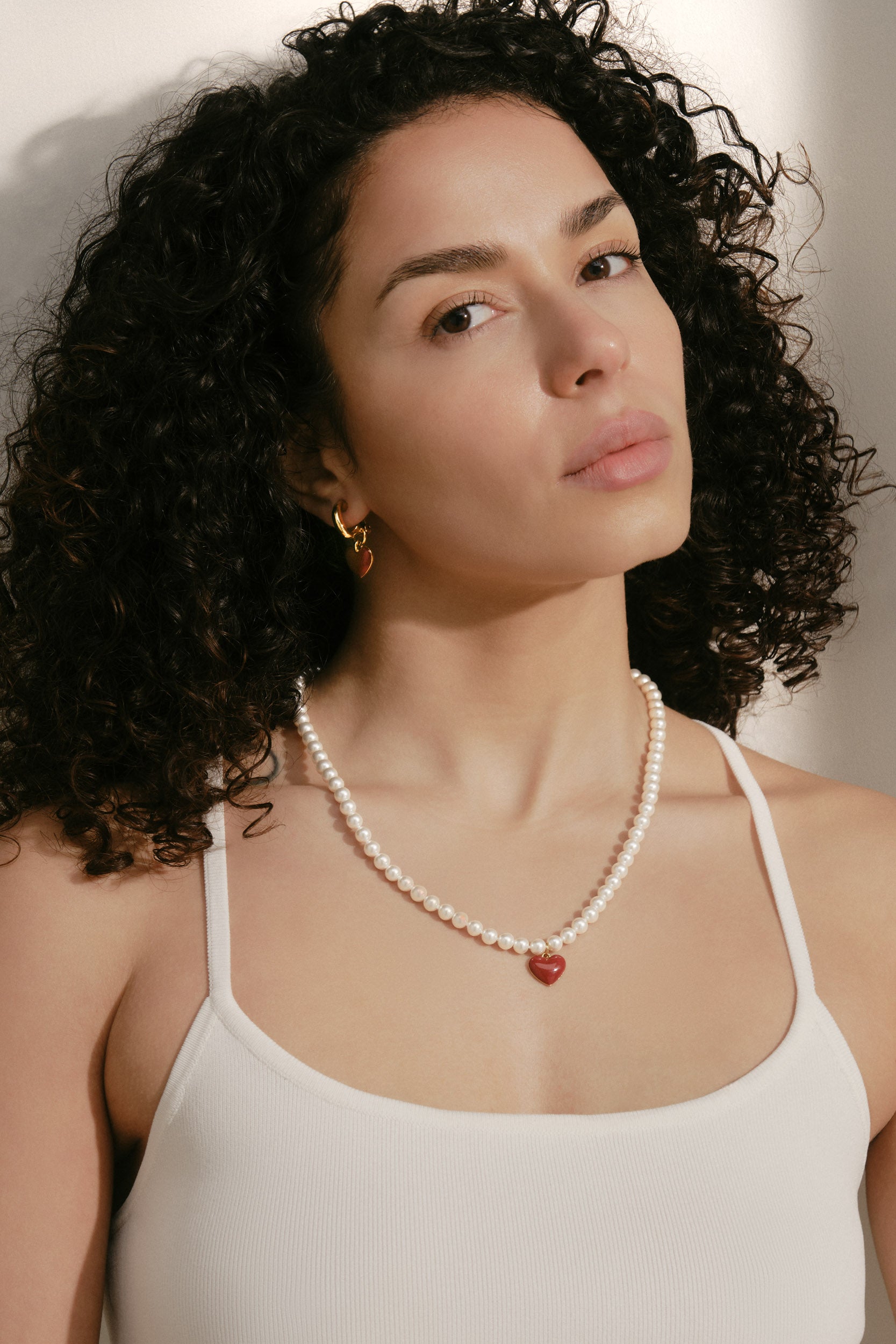 Woman wearing a pearl necklace with a heart pendant against a neutral background