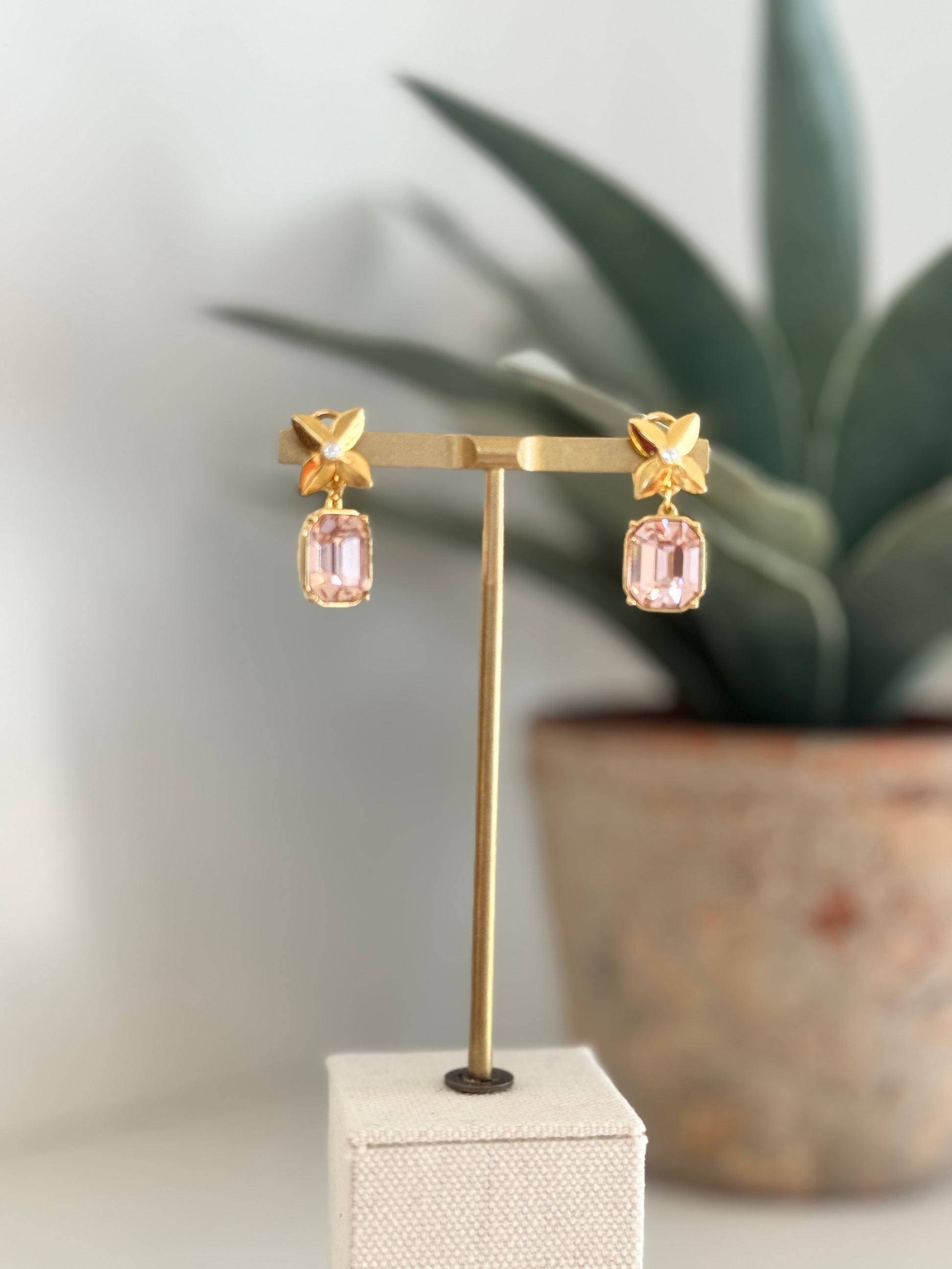 Gold earrings with pink gemstones on a stand with a plant in the background